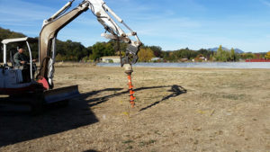 a backhoe with a screw bit digging holes